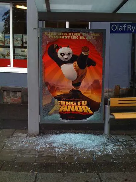 Een bushokje met een affiche van Kung Fu Panda waarvan de ruit is ingeslagen; het glas ligt in scherven op de stoep