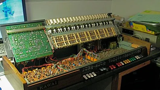 Het opengemaakte Kawai-orgel met een printplaat rechtop, de toetscontacten en een bos gekleurde draden