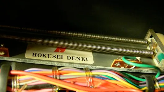 Detail in het orgel: een metalen plaatje met het opschrift HOKUSEI DENKI, tussen veren en gekleurde bedrading