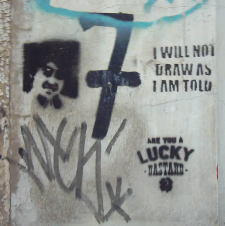Muur vol stencils: een gezicht met snor, een groot zwart kruis, de tekst I WILL NOT DRAW AS I AM TOLD en daaronder ARE YOU A LUCKY BASTARD
