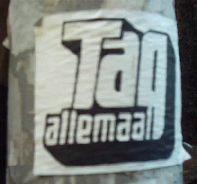 Een witte plaksticker met het logo Tag allemaal op een metalen paal